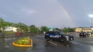 Police vehicle parked in a rain-soaked area with a rainbow in the background, representing New